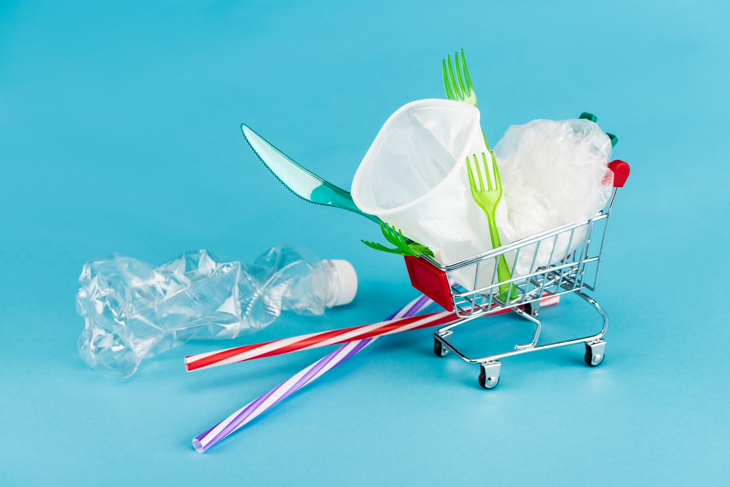 disposable plastic objects in small shopping cart on blue background