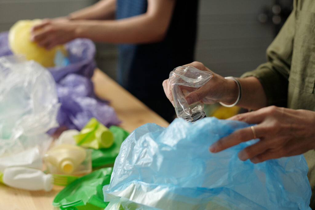 Hands of contemporary senior woman putting smashed plastic bottle into sack