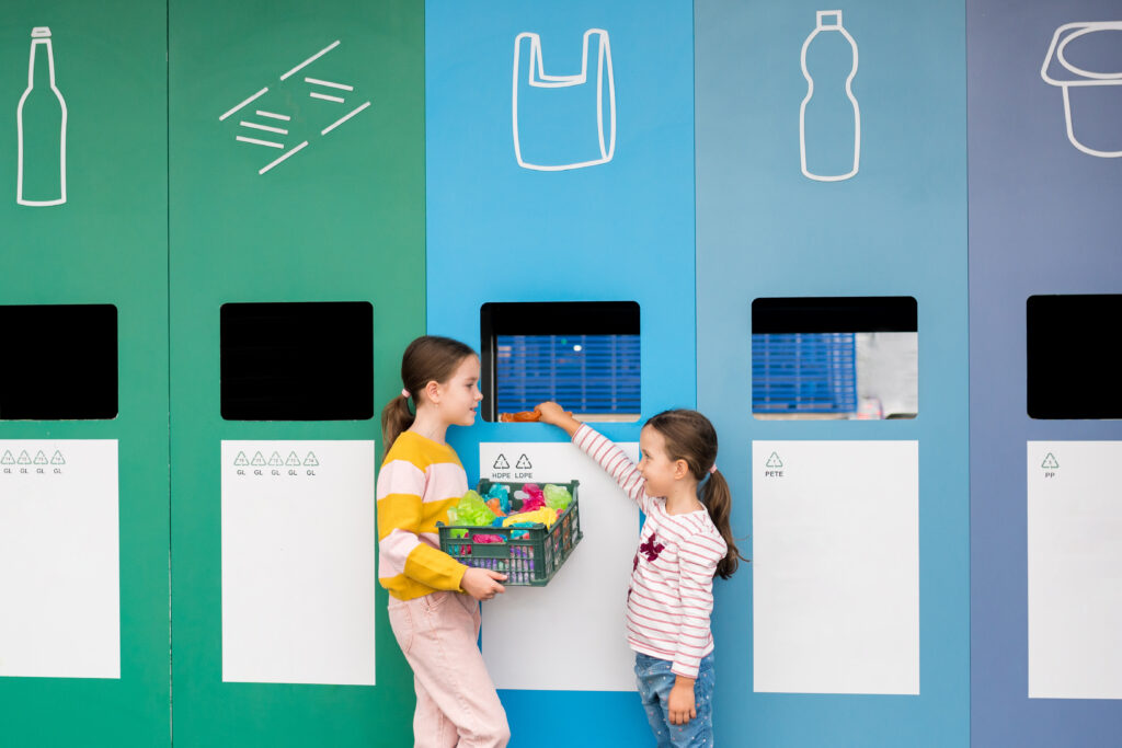 Girls taking out plastic trash in recycling centre. Children putting plastic bagwaste and PET bottle in recycling bin. Sustainble lifestyle concept. National recycling week.